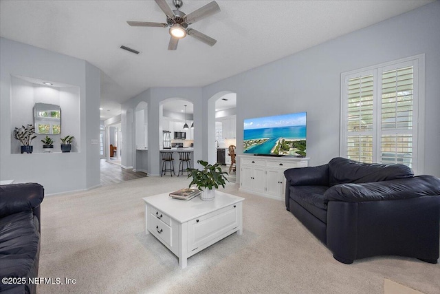 living area with light carpet, ceiling fan, arched walkways, and visible vents