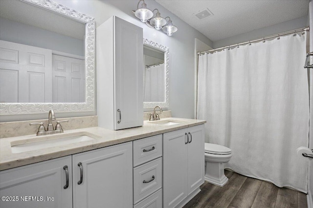 full bathroom with a textured ceiling, wood finished floors, a sink, and visible vents