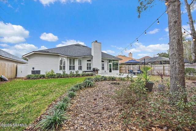 back of property featuring a chimney, fence, a lawn, and a patio