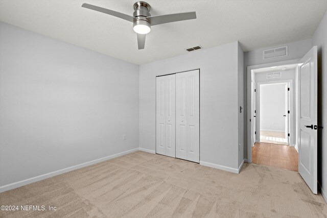 unfurnished bedroom with light colored carpet, ceiling fan, and a closet