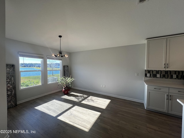 unfurnished dining area featuring a water view, an inviting chandelier, lofted ceiling, and dark hardwood / wood-style flooring