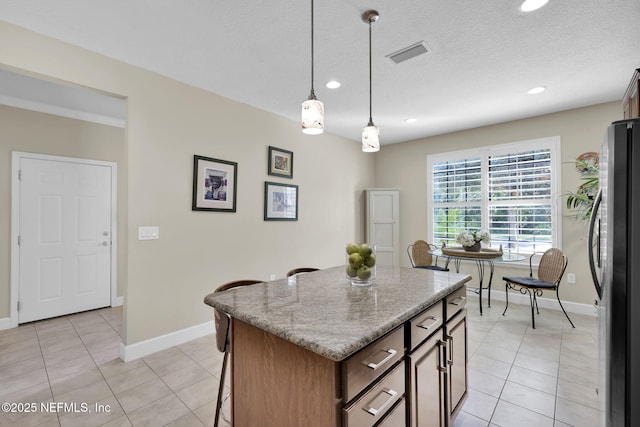 kitchen featuring hanging light fixtures, light tile patterned flooring, a center island, and stainless steel refrigerator