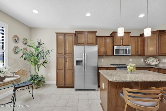 kitchen with pendant lighting, stainless steel appliances, light stone counters, tasteful backsplash, and a kitchen island