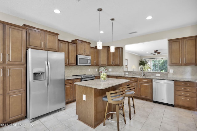 kitchen featuring sink, hanging light fixtures, stainless steel appliances, a center island, and light stone countertops