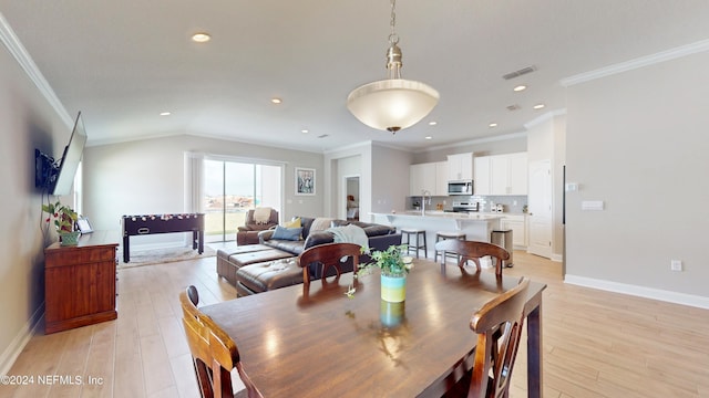 dining space featuring crown molding, vaulted ceiling, sink, and light hardwood / wood-style flooring