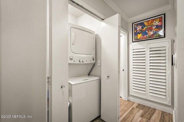 laundry area featuring crown molding, stacked washer and dryer, and light hardwood / wood-style flooring