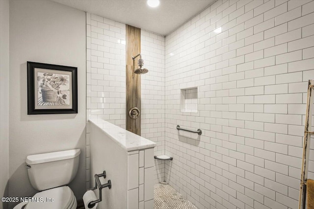 bathroom with a tile shower, a textured ceiling, and toilet