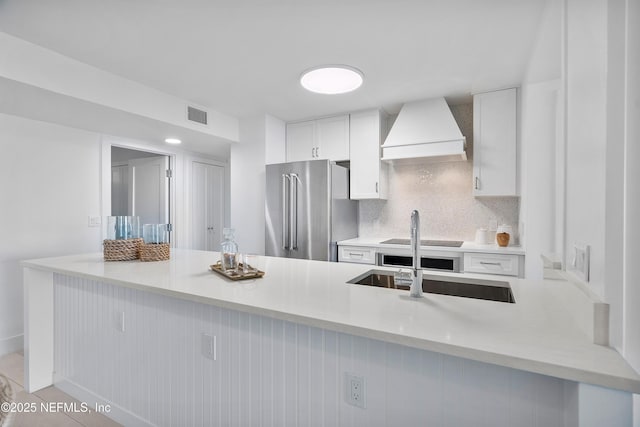 kitchen featuring tasteful backsplash, white cabinetry, custom range hood, and high end refrigerator