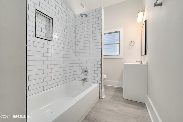 full bathroom with tiled shower / bath combo, vanity, hardwood / wood-style floors, and toilet