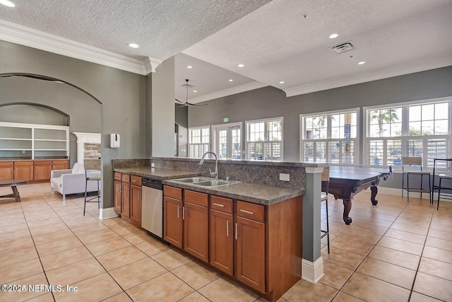 kitchen featuring light tile patterned flooring, a sink, stainless steel dishwasher, brown cabinets, and a kitchen bar