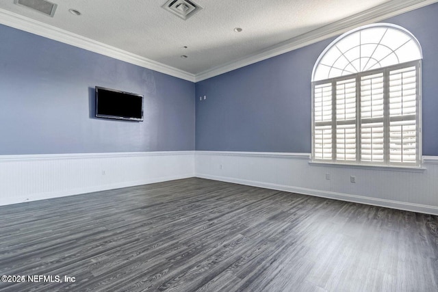 empty room with a wainscoted wall, dark wood finished floors, visible vents, ornamental molding, and a textured ceiling