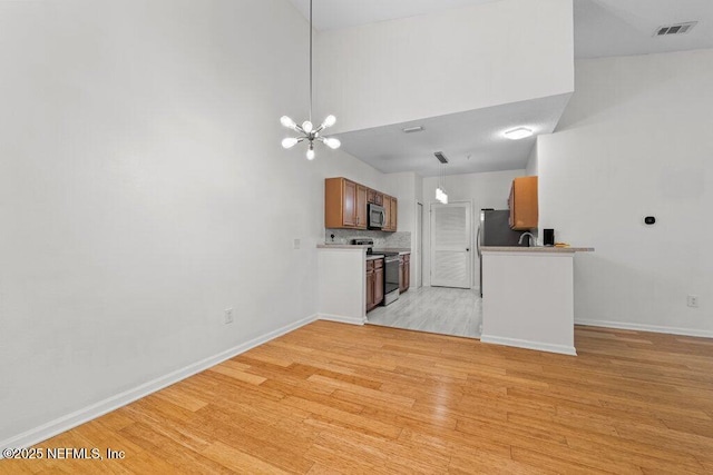 kitchen featuring brown cabinets, light wood finished floors, light countertops, backsplash, and appliances with stainless steel finishes