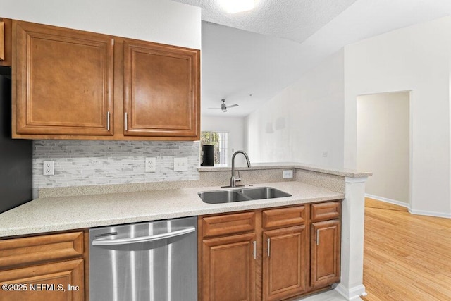 kitchen featuring brown cabinets, light countertops, backsplash, stainless steel dishwasher, and a sink