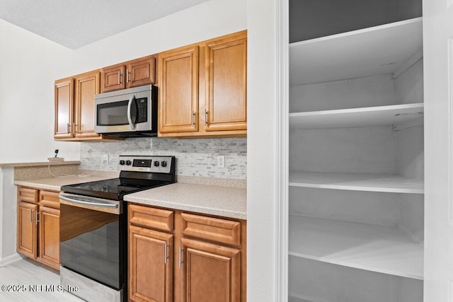 kitchen featuring stainless steel appliances, brown cabinetry, light countertops, and backsplash