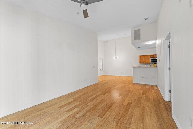 unfurnished living room with visible vents, a towering ceiling, light wood-style flooring, a ceiling fan, and baseboards