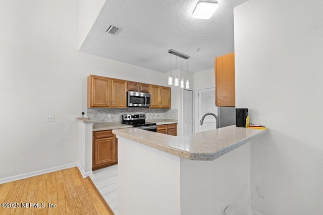 kitchen with light countertops, hanging light fixtures, appliances with stainless steel finishes, brown cabinetry, and a peninsula