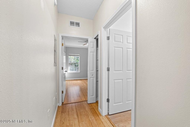 hallway with light wood-style flooring, visible vents, and baseboards