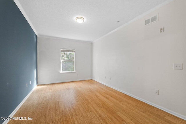 empty room featuring visible vents, light wood-style flooring, ornamental molding, a textured ceiling, and baseboards