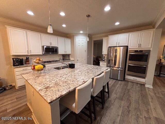 kitchen featuring pendant lighting, white cabinetry, stainless steel appliances, and an island with sink