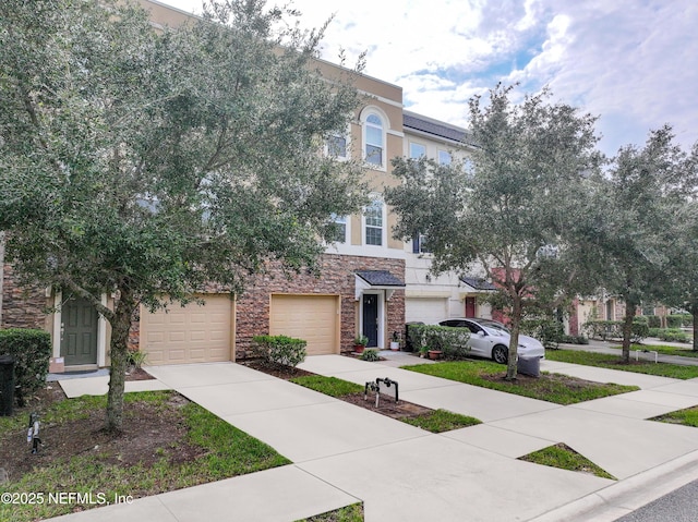 townhome / multi-family property featuring driveway, stone siding, an attached garage, and stucco siding