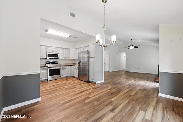 kitchen featuring vaulted ceiling, ceiling fan with notable chandelier, decorative light fixtures, stainless steel appliances, and light hardwood / wood-style flooring