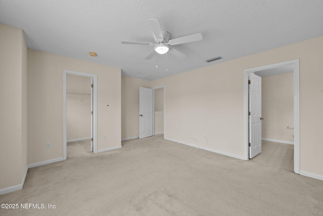 unfurnished bedroom with a spacious closet, ceiling fan, light carpet, a textured ceiling, and a closet