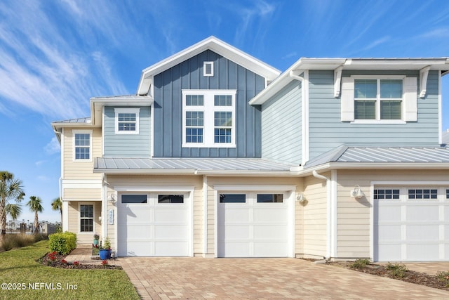 view of front of house featuring a standing seam roof, a garage, decorative driveway, board and batten siding, and metal roof