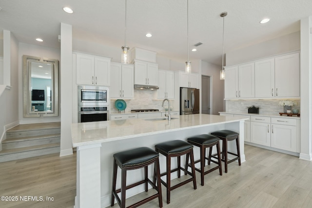 kitchen featuring under cabinet range hood, light wood-style flooring, appliances with stainless steel finishes, and a sink