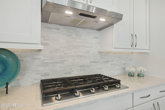 kitchen featuring backsplash, stainless steel gas cooktop, light stone counters, range hood, and white cabinetry