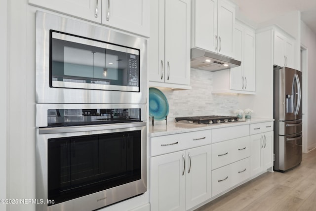 kitchen featuring under cabinet range hood, appliances with stainless steel finishes, white cabinets, light wood finished floors, and decorative backsplash