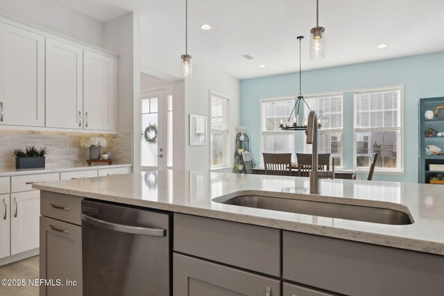 kitchen featuring light stone counters, a sink, stainless steel dishwasher, decorative light fixtures, and tasteful backsplash