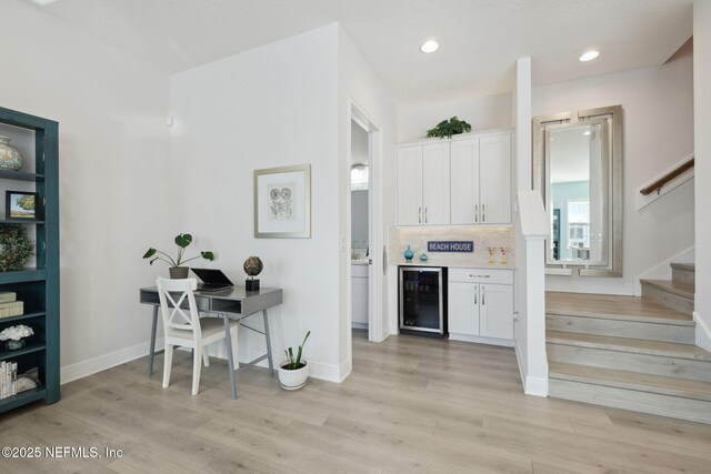 bar with stairway, beverage cooler, a dry bar, and light wood-style flooring