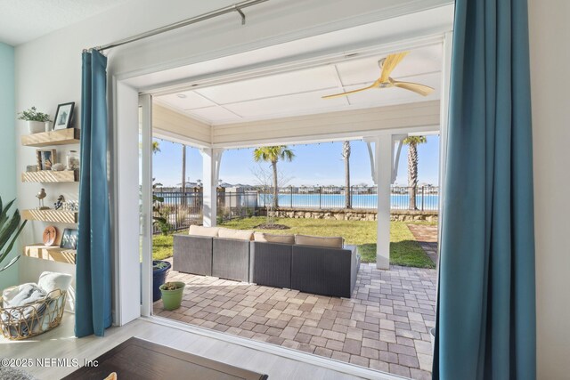 doorway to outside featuring wood finished floors, a sunroom, a ceiling fan, and a water view