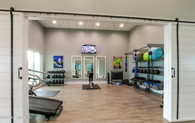 gym featuring a barn door, wood finished floors, baseboards, and a towering ceiling