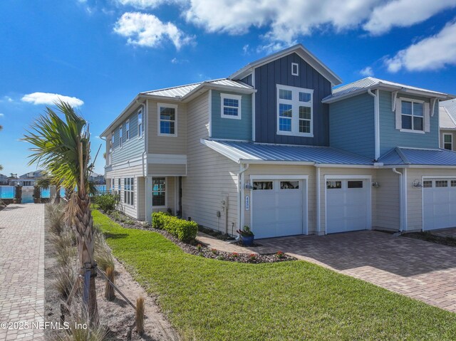 view of front of house featuring a front yard, a standing seam roof, a garage, decorative driveway, and board and batten siding