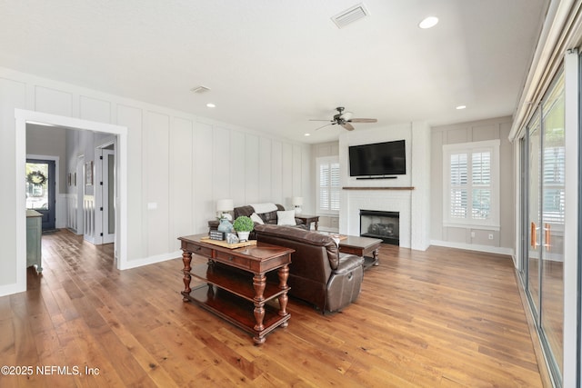 living room featuring ceiling fan, a large fireplace, light hardwood / wood-style flooring, and a wealth of natural light