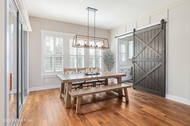 dining area with a barn door, hardwood / wood-style floors, and an inviting chandelier