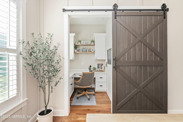 office space with a barn door, built in desk, and light hardwood / wood-style flooring