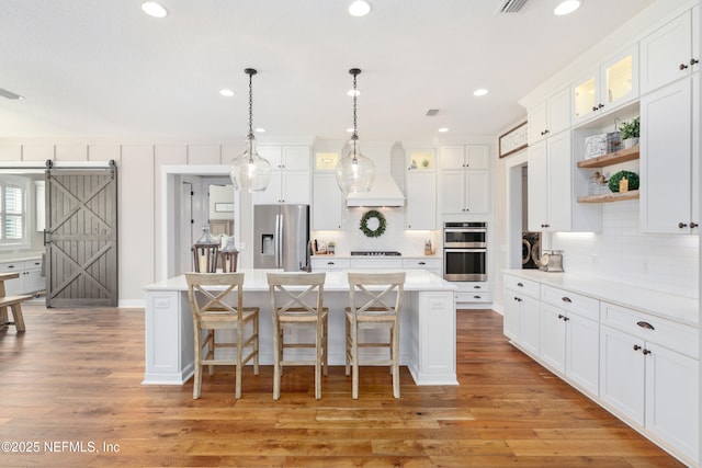 kitchen featuring a barn door, white cabinetry, appliances with stainless steel finishes, and custom range hood