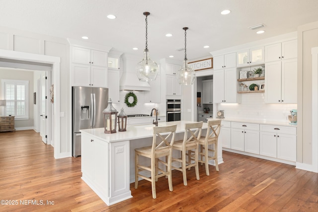 kitchen with premium range hood, stainless steel appliances, a center island with sink, and white cabinets