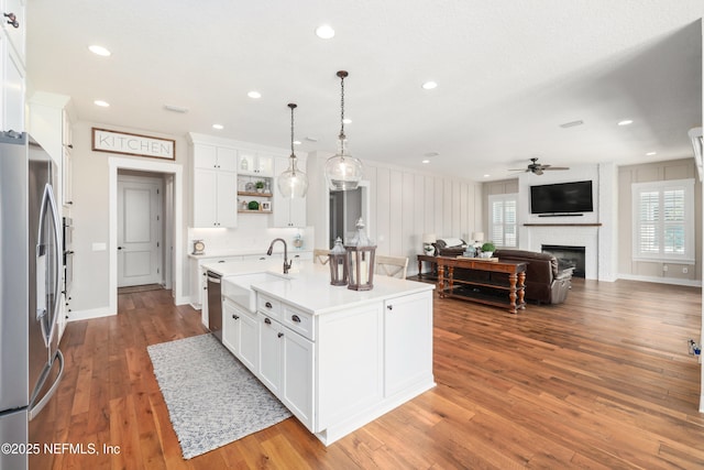 kitchen featuring appliances with stainless steel finishes, pendant lighting, an island with sink, white cabinets, and a brick fireplace