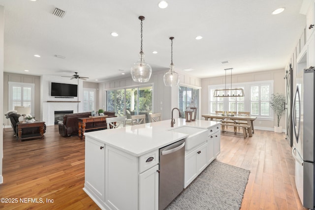 kitchen with sink, white cabinetry, decorative light fixtures, appliances with stainless steel finishes, and an island with sink