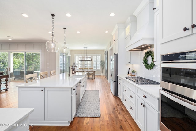 kitchen with custom exhaust hood, an island with sink, white cabinetry, and stainless steel appliances