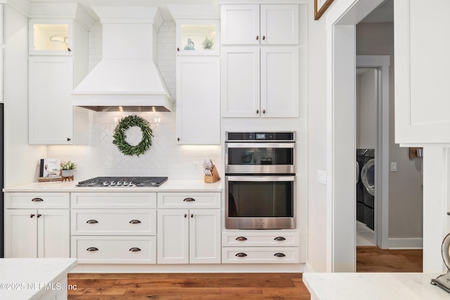 kitchen featuring white cabinetry, stainless steel appliances, custom exhaust hood, and backsplash