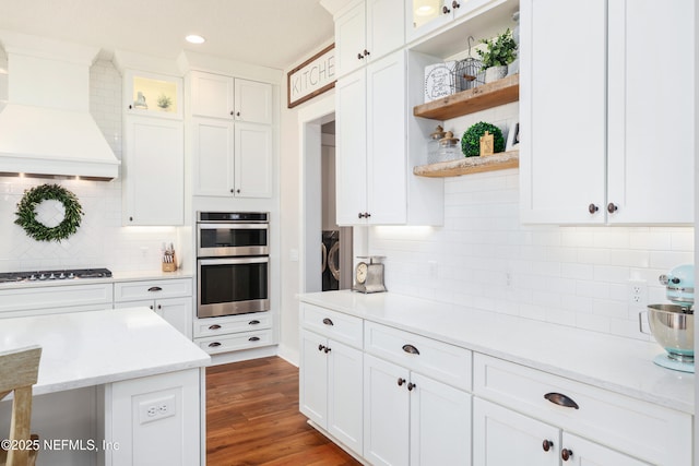 kitchen featuring gas cooktop, premium range hood, light stone countertops, white cabinets, and stainless steel double oven