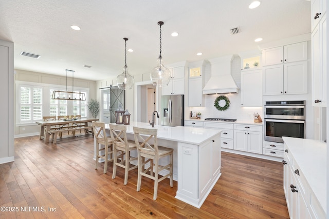 kitchen featuring premium range hood, a breakfast bar area, an island with sink, stainless steel appliances, and a barn door