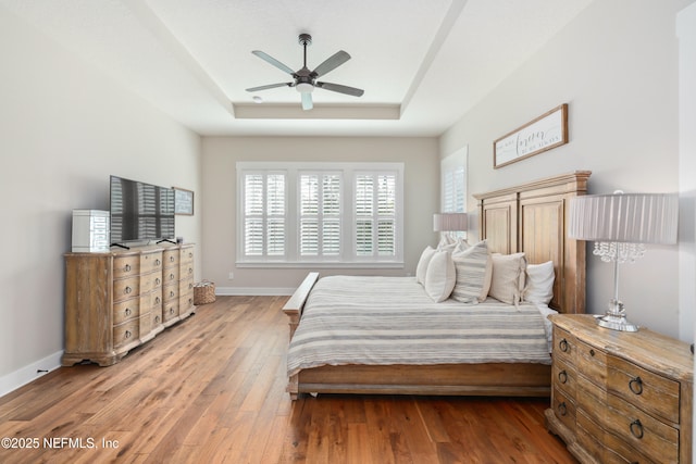 bedroom with ceiling fan, a raised ceiling, and light hardwood / wood-style flooring