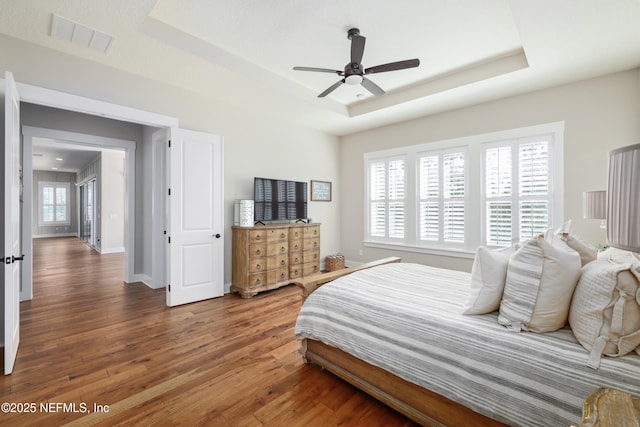 bedroom with a tray ceiling, dark wood-type flooring, and ceiling fan