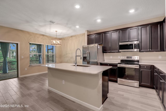 kitchen with appliances with stainless steel finishes, sink, hanging light fixtures, and a center island with sink