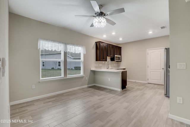 kitchen featuring a kitchen bar, light hardwood / wood-style flooring, dark brown cabinetry, and kitchen peninsula